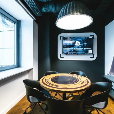 Modern furnished conference room at Konstruktorska 11, Warsaw Mokotow, featuring a round table, chairs, a wall-mounted screen, and a flip chart. Ideal office space rental for meetings.