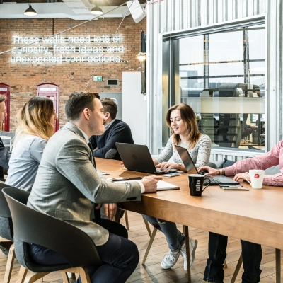 Group of people engaged in a meeting around a large wooden table in a modern office space at Al. Jerozolimskie 181B, Warsaw Ochota, available for office space rental.