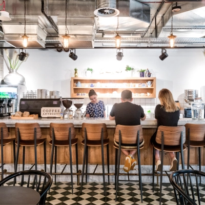 A modern office lounge at Koszykowa 61, Warsaw Śródmieście, featuring a bar counter with three people engaged in conversation, ideal for casual meetings and office space rental.