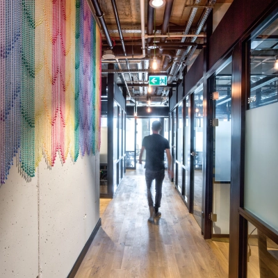 Man walks down a modern office hallway in Koszykowa 65, Warsaw Śródmieście, featuring colorful wall art and industrial design, perfect for office space rental.