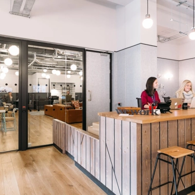 Inside an office space rental at Krakowskie Przedmieście 13, Warsaw Śródmieście, featuring a reception area with wooden seating and three people discussing work.