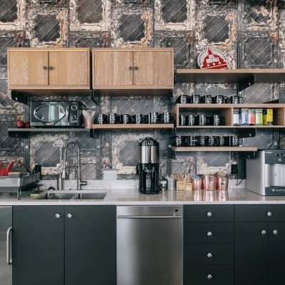 A modern kitchenette in an office space with coffee machines, shelves, and a stainless steel sink, ideal for office space rental in Warsaw Śródmieście.