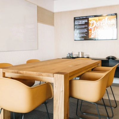 Furnished office space at Krakowskie Przedmieście 13 in Warsaw Śródmieście, featuring a wooden table and yellow chairs under a wall-mounted screen, ideal for office space rental.