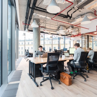 Modern workspace at Krucza 50, Warsaw Śródmieście, featuring large windows and professionals engaged in business activities. Ideal office space rental opportunity with sleek interiors.