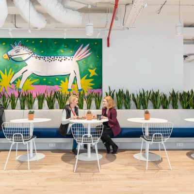 People engaged in discussion at tables in a stylish, furnished office space with vibrant wall art at Krucza 50, ideal for office space rental in Warsaw Śródmieście.