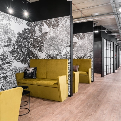 Modern office space in Warsaw's Śródmieście featuring stylish yellow seating, floral wall art, and a sleek hallway enhancing the office space rental experience.