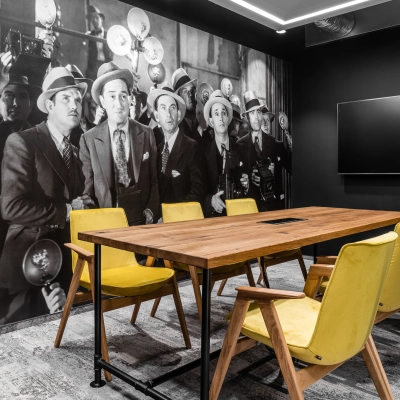 Furnished conference room with a large wooden table, yellow chairs, and a wall mural of photographers, ideal for office space rental.