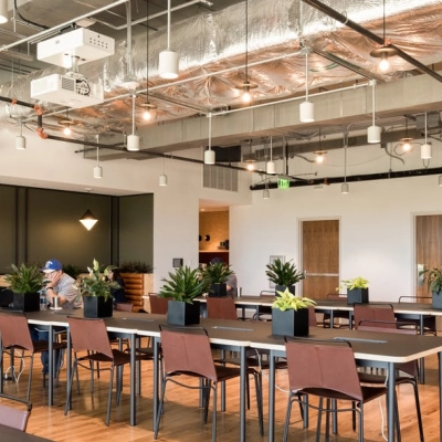 Modern office space rental in Warsaw Wola at Grzybowska 60 featuring open workspaces with stylish lighting and plants, two individuals working at separate tables.