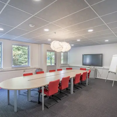 Modern conference room at Molenweer 2, Wateringen, available for office space rental with a large table, red chairs, smart board, and natural lighting.