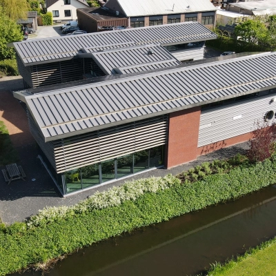 Exterior view of a modern office building at M.A. Reinaldaweg 2d, Woerden, featuring sleek architectural lines, surrounded by greenery and a waterway, ideal for rent office space.