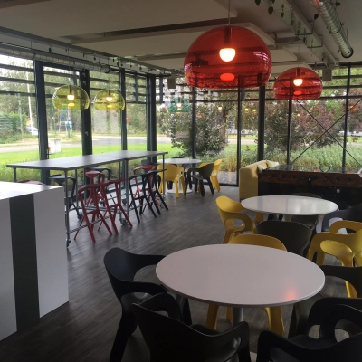 A modern, furnished office space with colorful seating and large windows in Woerden, ideal for rent office space seekers. The room is bright and versatile, featuring communal tables and comfortable chairs.