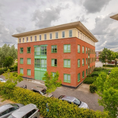 Exterior view of Mercurion 24 in Zevenaar, showcasing the brick and green facade with parked cars in front, ideal for office space rental.