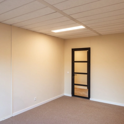 Empty office space at Mercurion 24, Zevenaar, ready for rent. Features beige walls and a simple carpeted floor, ideal for personalizing your workspace.