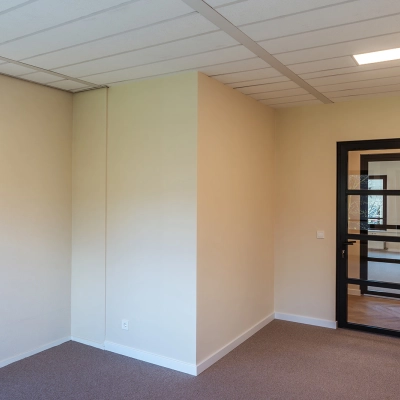 Empty office space with beige walls and carpet, featuring a black-framed glass door at Mercurion 24, Zevenaar, available for office space rental.