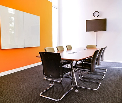 Modern conference room with an orange accent wall and a long table surrounded by chairs, located at Badenerstrasse 47 in Zürich Center. Ideal for office space rental.