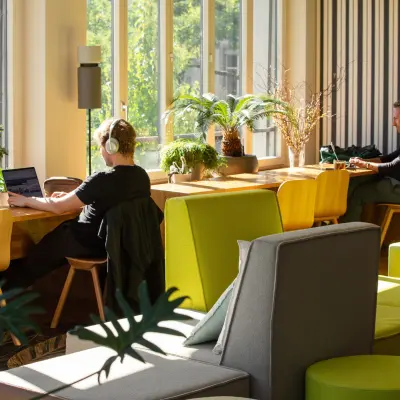 Bright office space with individuals working on laptops at a wooden table surrounded by greenery, perfect for office space rental at Ernst Nobs Platz 1, Zürich Center.