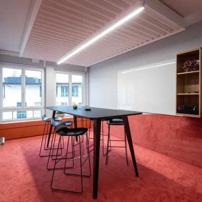 Stylish office space with a red carpet, high table, and modern stools, located at Talacker 41 in Zürich Center. Ideal for office to rent needs.