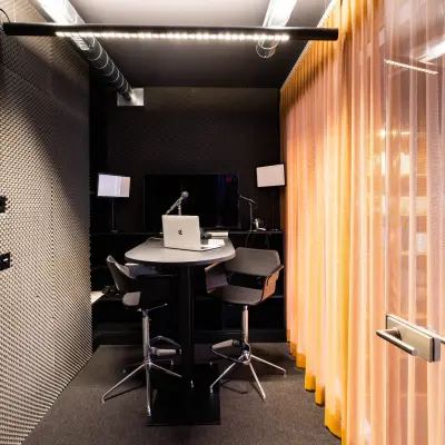 Modern office space with soundproof walls, featuring high stools and a central desk with monitors.