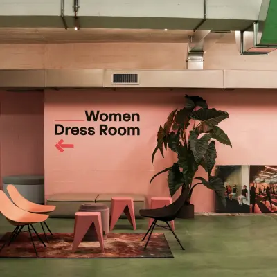 A modern office space with colorful seating, green flooring, and pink walls featuring a sign for a Women's Dress Room, ideal for office space rental.