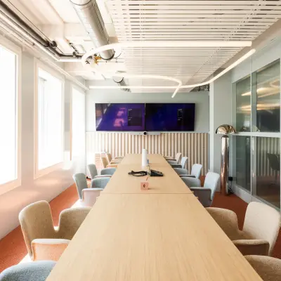 Bright, modern conference room at Stockerstrasse 33, Zürich Enge, featuring a long wooden table surrounded by chairs, large windows, and a mounted screen, ideal for office space rental.