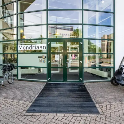 Exterior view of an office building at Dokter van Deenweg 1, Zwolle, highlighting the entrance with glass facades and a mix of bikes and scooters parked outside.