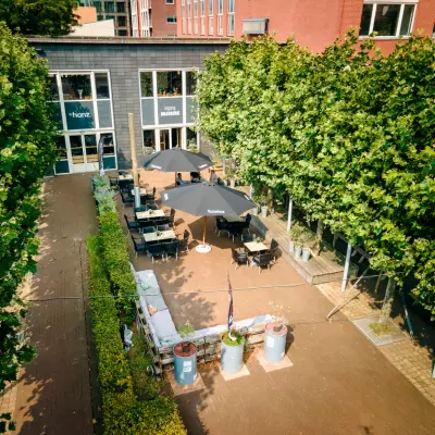 Exterior view of Hanzeplein 11-27 Zwolle with outdoor seating, ideal for office space rental among leafy trees.