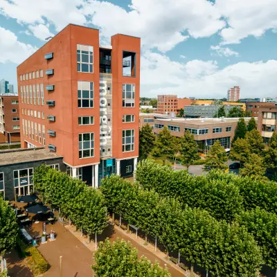 Exterior view of the office building at Hanzeplein 11-27, Zwolle, showcasing a modern structure with surrounding greenery, available for office space rental.