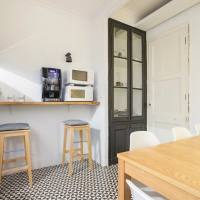 Espaciosa área de descanso en alquiler de oficinas en Barcelona Eixample, con mesas de madera y zona de café, iluminación natural y decoración moderna.