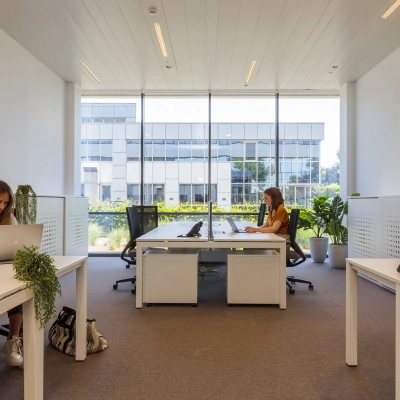 Kantoorruimte huren in Aalst met grote ramen en moderne inrichting, waar twee personen aan bureaus werken op laptops.