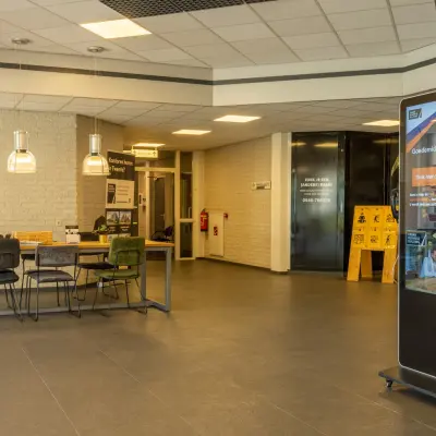 Ruime entree van een kantoorpand op Bedrijvenpark Twente 305, Almelo, met moderne meubels en een informatiescherm. Ideaal voor wie kantoorruimte wil huren in een inspirerende omgeving.