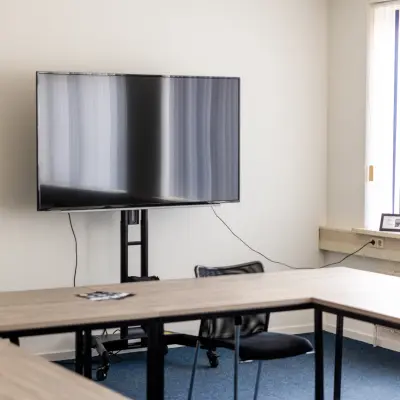 Kantoorruimte te huur op Bedrijvenpark Twente 305 in Almelo, met houten tafels, een grote televisie aan de muur en veel natuurlijk licht door het raam.