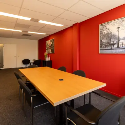 Vergaderruimte in kantoorpand Bedrijvenpark Twente 305, Almelo, met rode muur en houten tafel omringd door stoelen. Ideaal voor kantoorruimte huren.