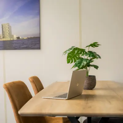 Kantoorruimte huren in Almere Stad aan Markerkant 1310 met een tafel, stoelen, een laptop en een plant. De muren zijn voorzien van fotokunst.