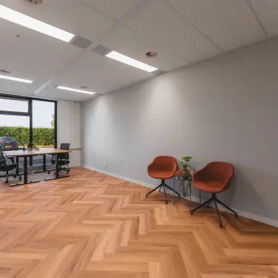 Moderne kantoorruimte te huur in Almere Stad met grote ramen, houten vloer en enkele meubels, ideaal voor zakelijke activiteiten.