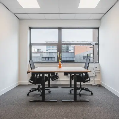 Kantoorruimte te huur in Almere Stad, Veluwezoom 15, met twee bureaus en stoelen onder een raam met uitzicht op naastgelegen kantoorpanden.