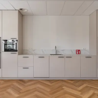 Heldere kantoorruimte in Almere Stad met moderne keuken, ideaal voor kantoorruimte huren. Strakke opstelling met houtpatroon vloer, witte kasten en ingebouwde apparatuur.