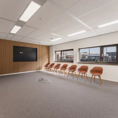 Moderne kantoorruimte op Veluwezoom 15 in Almere Stad met strakke lijnen, houten accenten en een rij stijlvolle stoelen langs de muur. Klaar voor vergaderingen of flexibele werkplekken.