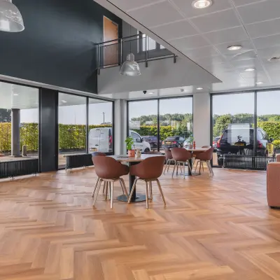 Lichte kantoorruimte met grote ramen en een parketvloer, ingericht met tafels en stoelen op Veluwezoom 15, Almere Stad. Ideaal voor wie kantoorruimte wil huren in een inspirerende omgeving.