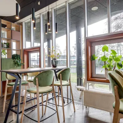 Moderne kantoorruimte huren in kantoorpand Maanlander 47, Amersfoort Calveen. Grote ramen laten veel licht binnen, met groen en hoge tafels in een uitnodigende omgeving.