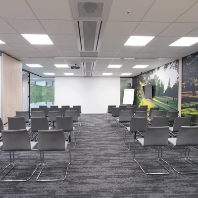 Moderne vergaderruimte met grijze stoelen en glazen wanden, geschikt voor kantoorruimte huren. Grote ramen laten veel licht binnen en er is een scherm voor presentaties.