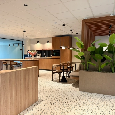 Moderne kantoorruimte in Amstelveen met houten en groene accenten, geschikt om te huren. Open werkruimte met stijlvolle meubels, planten en een kitchenette.