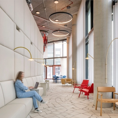Lichte en moderne lounge in een kantoorpand aan H.J.E. Wenckebachweg 230-258, Amsterdam met gedempte verlichting en stijlvolle zitbanken. Een persoon werkt op een laptop, wat de zakelijke sfeer benadrukt.