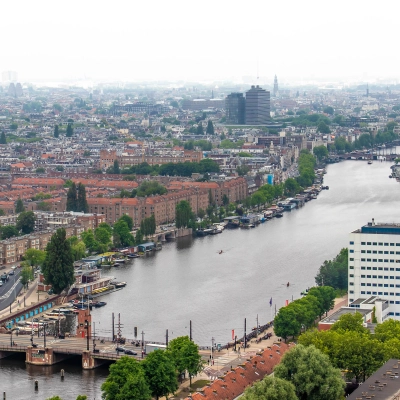Uitzicht op Amstelplein 8 in Amsterdam Amstel, met de rivier en de stad op de achtergrond. Een kantoorpand is zichtbaar nabij het water.