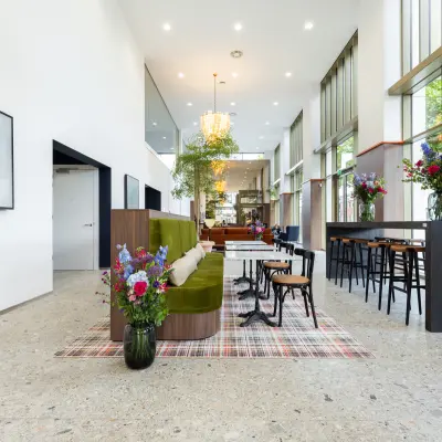 Moderne kantoorruimte met hoge plafonds en veel lichtinval, gelegen aan Willem Fenengastraat 16, Amsterdam Amstel. Ruimte is stijlvol gemeubileerd met banken en hoge tafels, ideaal voor huur als kantoorpand.