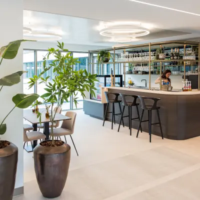 Moderne kantoorruimte huren op Walborg 2A in Amsterdam Buitenveldert, met een stijlvolle bar, grote planten en een vrouw die achter de balie bezig is.