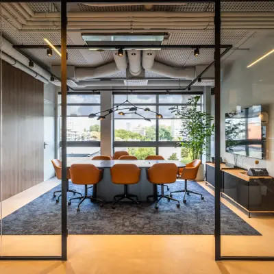 Vergaderruimte in kantoorpand met lange tafel, bruine leren stoelen en groot raam met uitzicht op Amsterdam Buitenveldert. Modern interieur met glazen wanden en houten accenten, geschikt voor kantoorruimte huren.