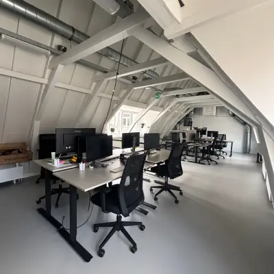 Moderne kantoorruimte te huur in Amsterdam Centrum, gelegen op Kloveniersburgwal 131K, ingericht met bureaus en computerschermen onder een karakteristiek schuin dak.