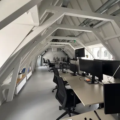 Moderne kantoorruimte huren aan de Kloveniersburgwal 131K in Amsterdam Centrum, met werkplekken onder karakteristieke balken, voorzien van bureaus en stoelen.