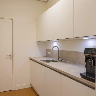Moderne pantry in kantoorpand op Korte Leidsedwarsstraat 133A, Amsterdam Centrum, met witte kasten en espressomachine, ideaal voor huur in deze kantoorruimte.