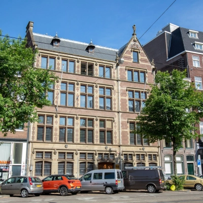 Buitenkant van een indrukwekkend historisch kantoorpand aan de Nieuwezijds Voorburgwal 104-108 in Amsterdam Centrum, ideaal voor kantoorruimte huren met klassieke architectuur en groene bomen langs de straat.